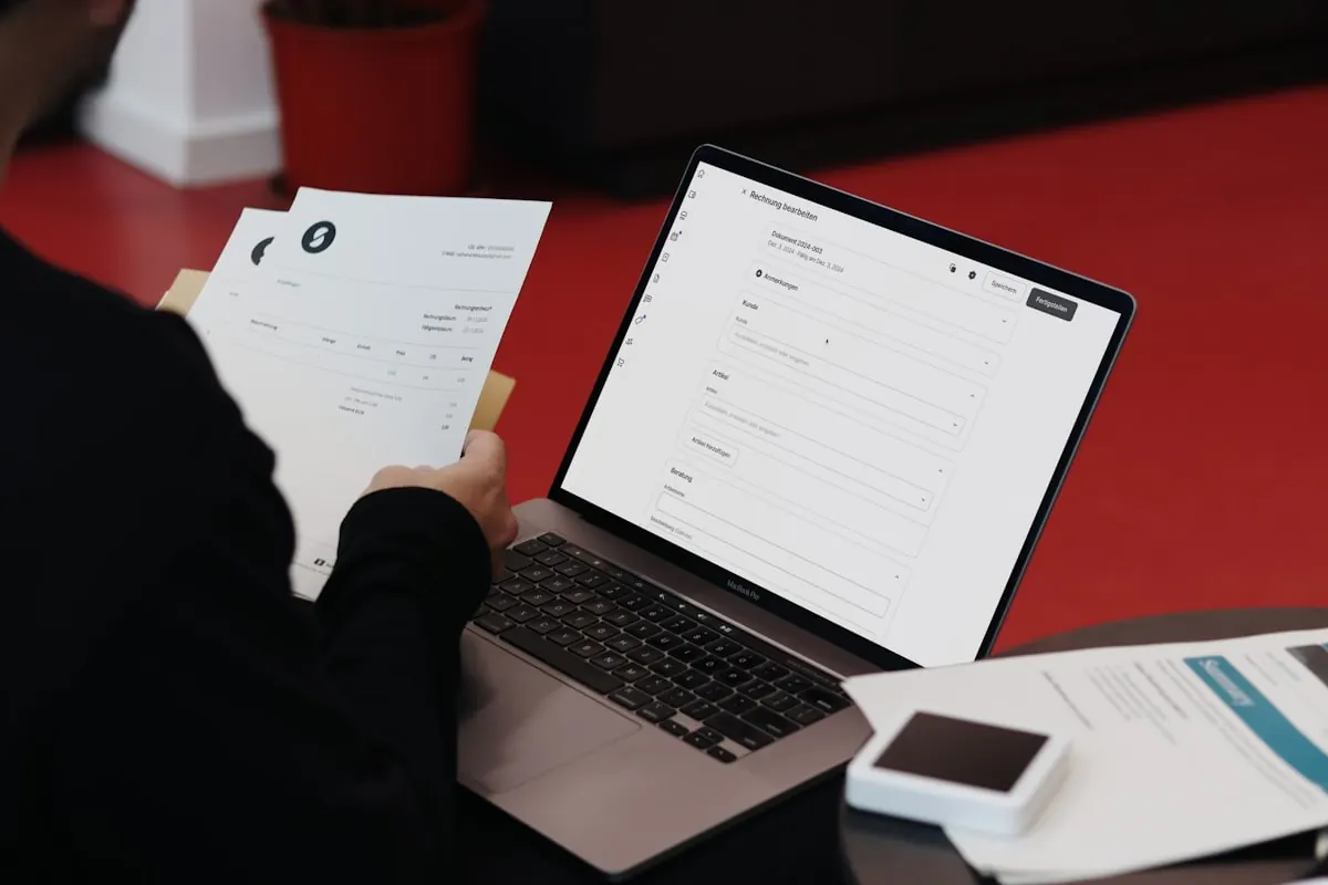 Person reviewing paper documents beside an open laptop