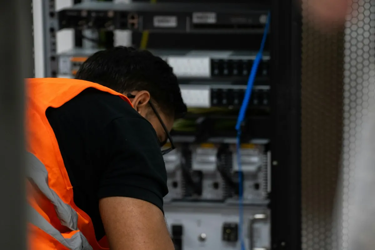Technician in a high-visibility vest working on equipment in a server rack