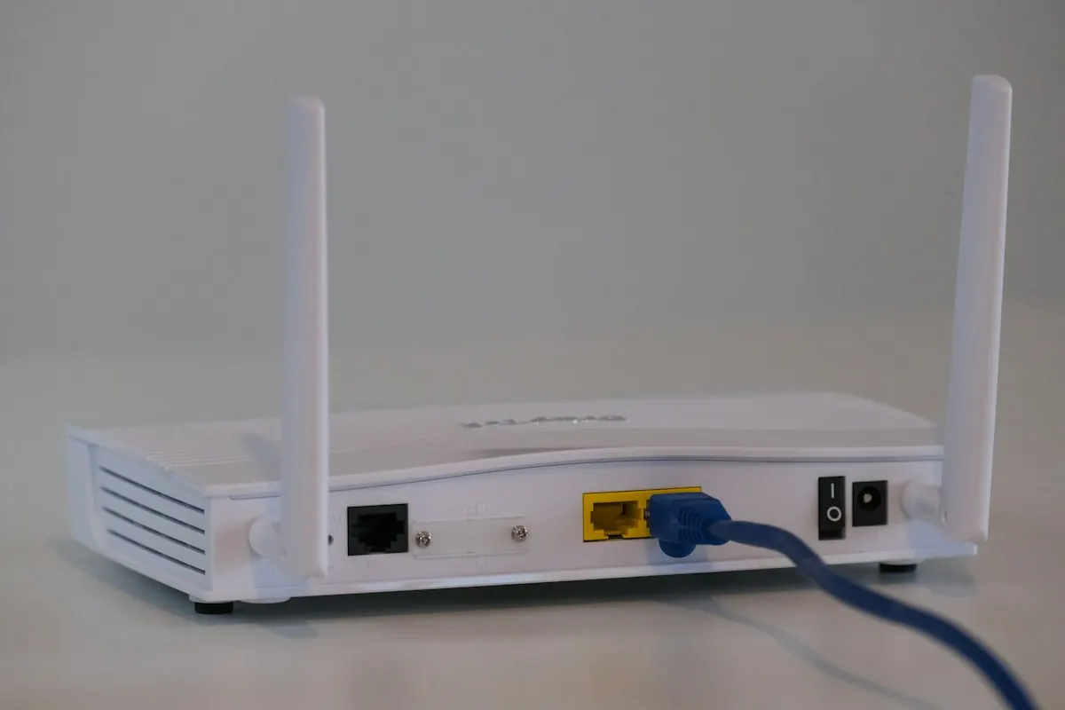 White wireless router with antennas and a blue network cable plugged in
